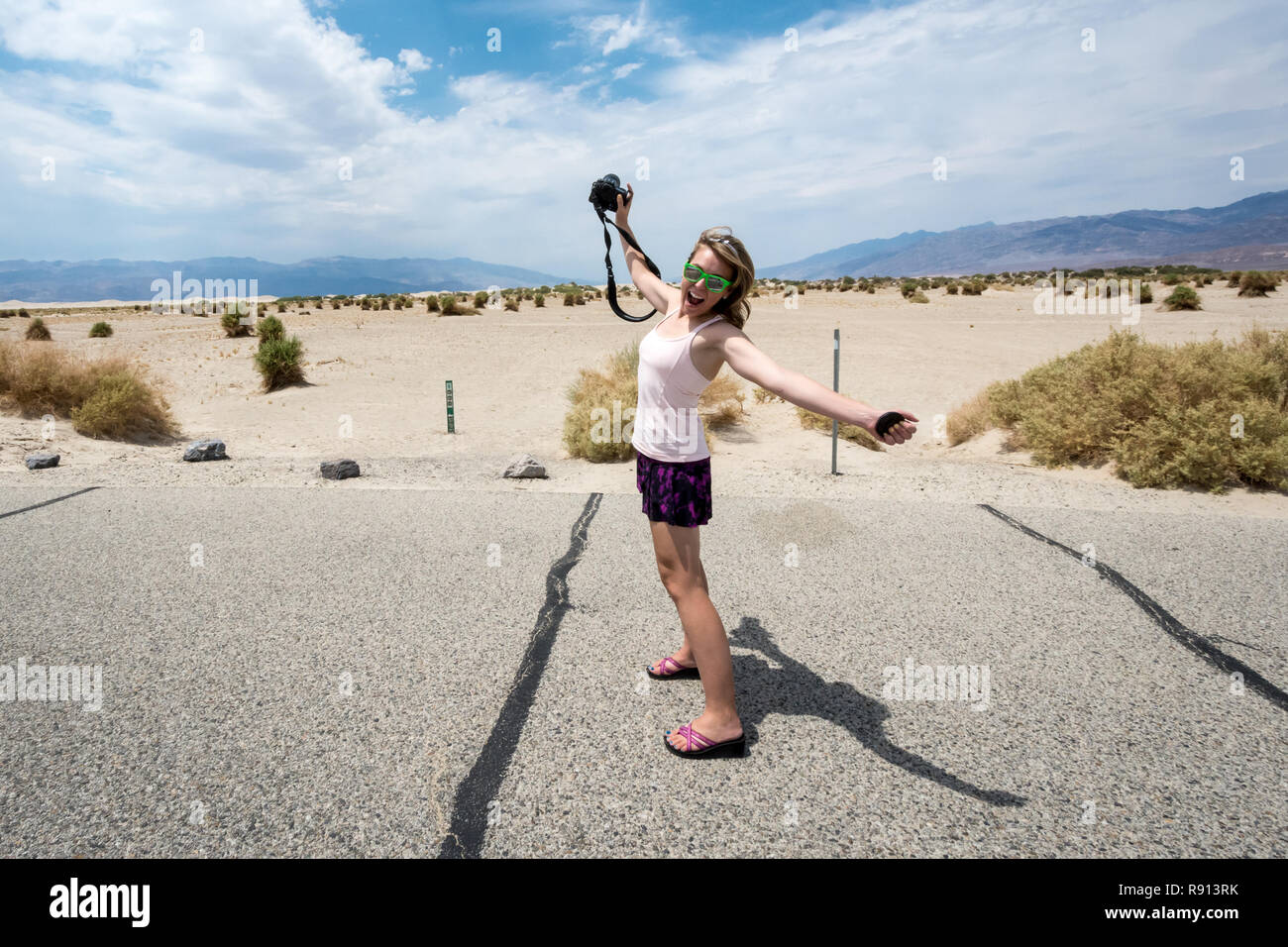 Hembra adulta joven fotógrafo en un viaje por carretera a través del Parque Nacional Valle de la muerte, se levanta y se estira sus brazos y piernas Foto de stock