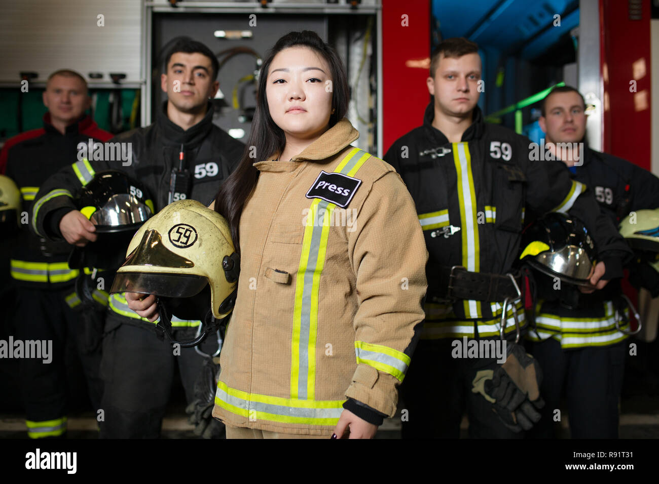 Retrato de cuatro jóvenes varones y mujeres bomberos en el fondo de un camión de bomberos Foto de stock