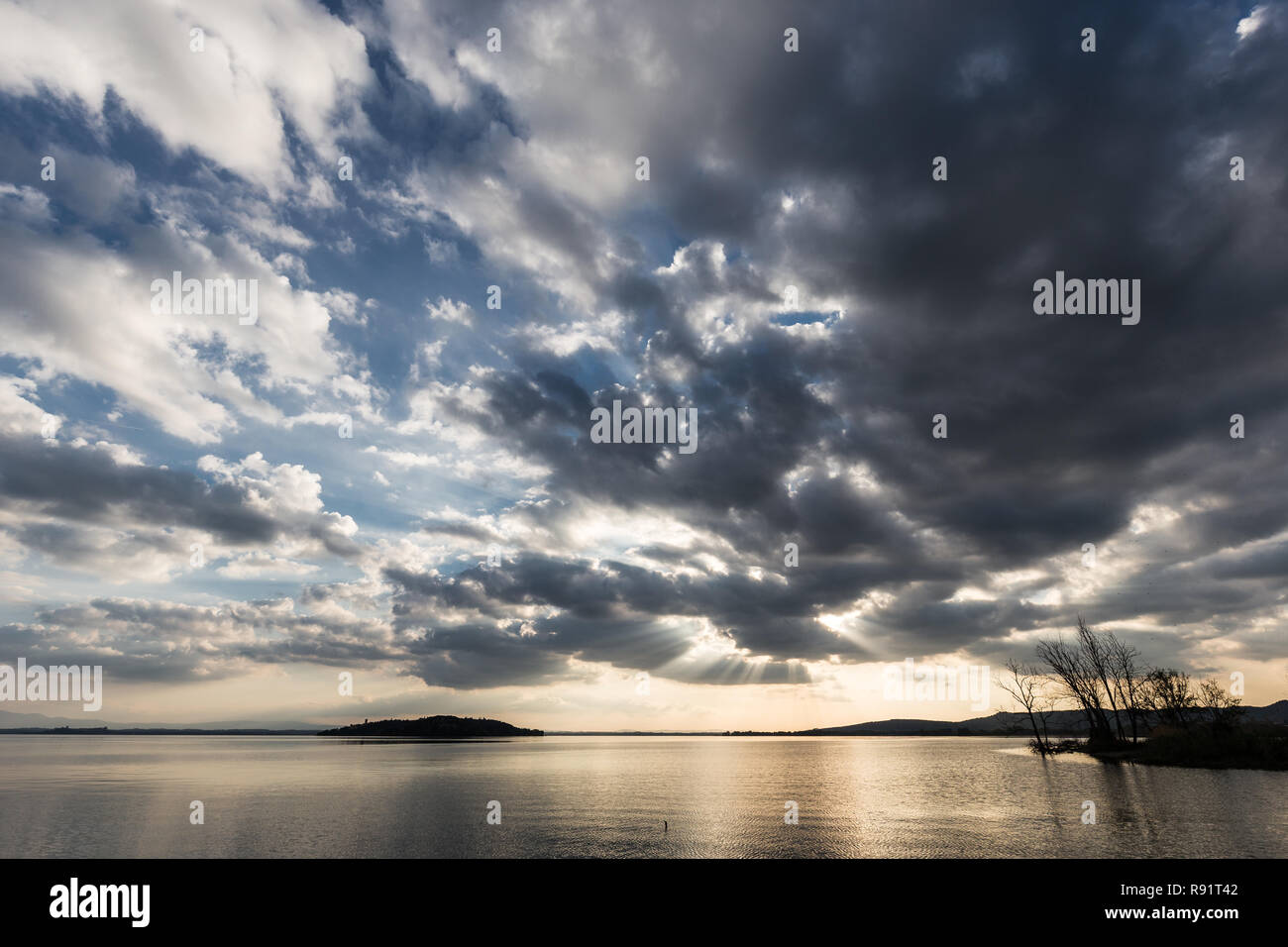 Hermosa vista de gran angular de un lago, con un inmenso cielo con nubes al atardecer sobre los árboles del esqueleto Foto de stock