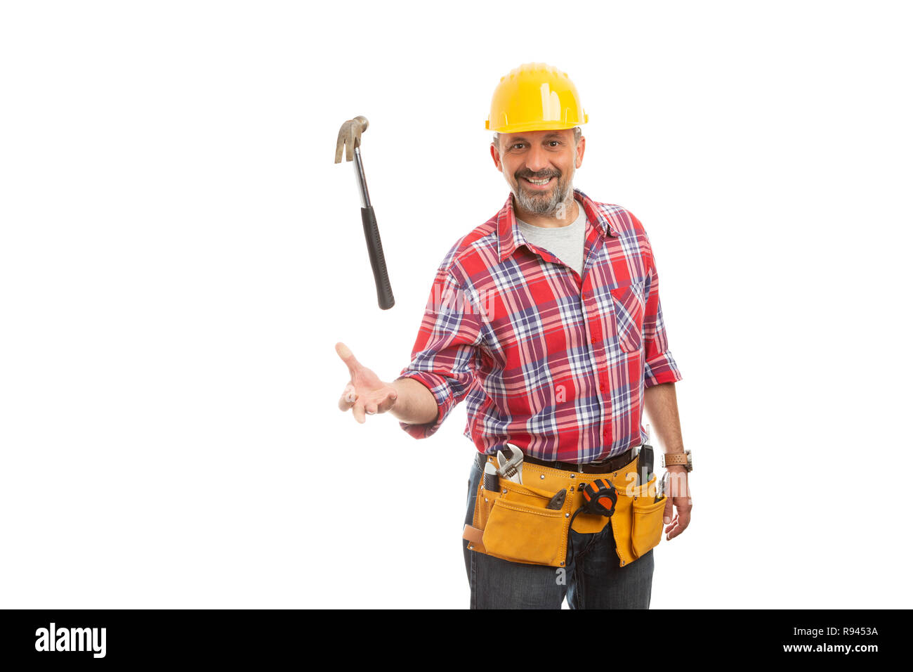 Constructor macho sonriente lanzando el martillo en el aire como truco con expresión amable aislado en blanco Foto de stock