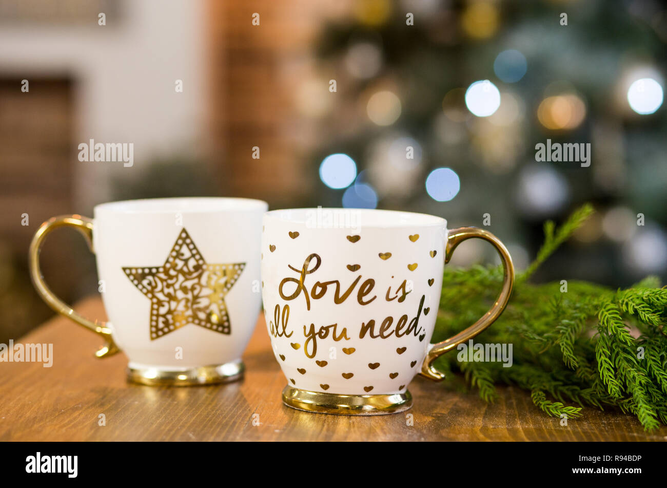 Dos tazas en blanco con texto romántico en Navidad con luces interiores en segundo plano. Foto de stock