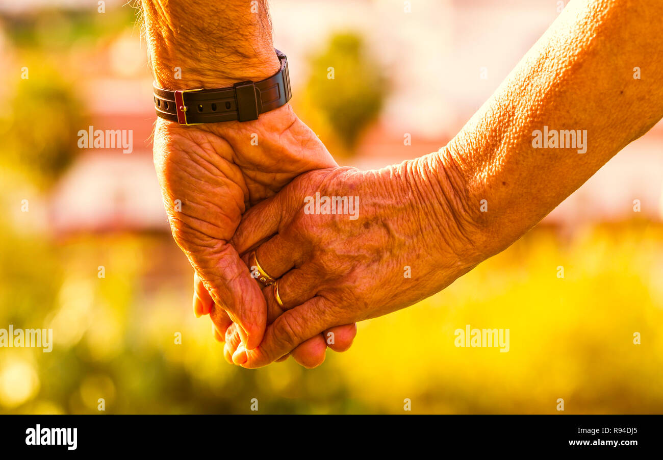 Captura recortada de la pareja de ancianos tomados de la mano exterior con la luz del atardecer. Se centran en las manos Foto de stock