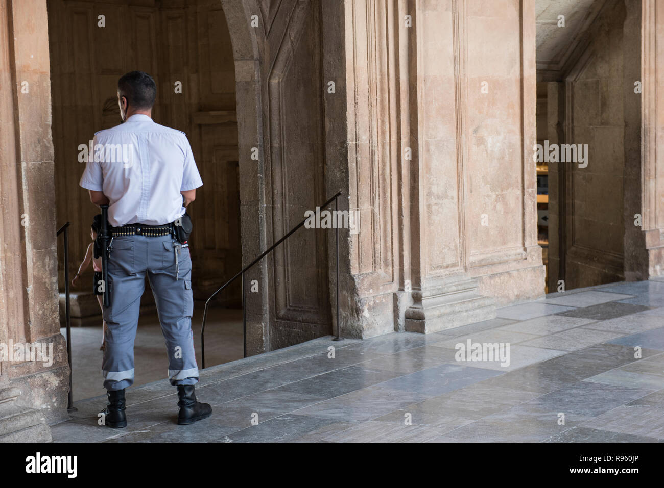 Alhambra Palace guardia de seguridad vigilando durante el día. El COP es  visto en uniforme de camisa blanca y pantalón gris. Él se inclina contra el  Fotografía de stock - Alamy