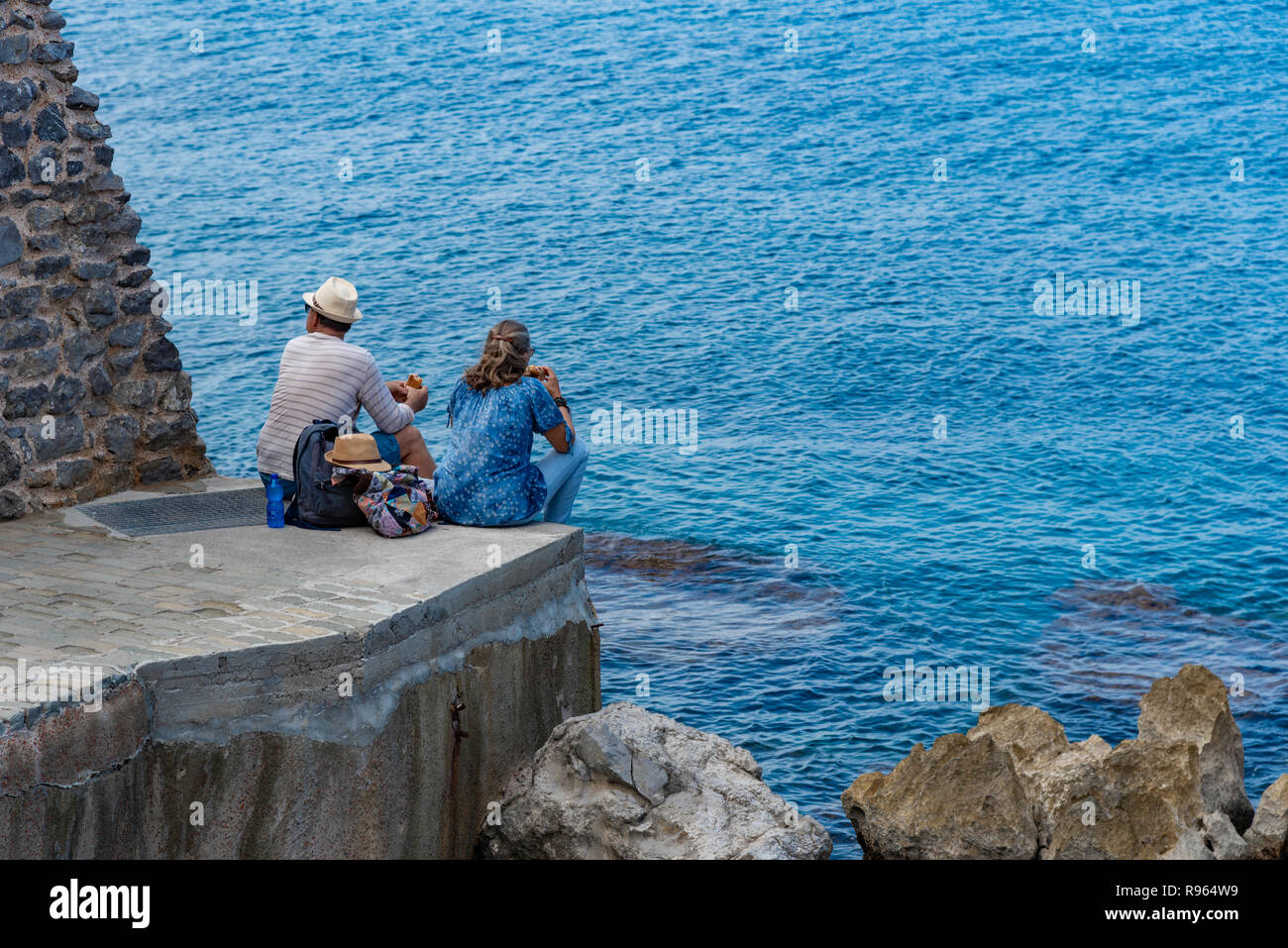 Pareja de hombre y mujer en la orilla del mar disfrutando de la vista del mar en la ciudad de Cefalu, Sicilia, isla Foto de stock