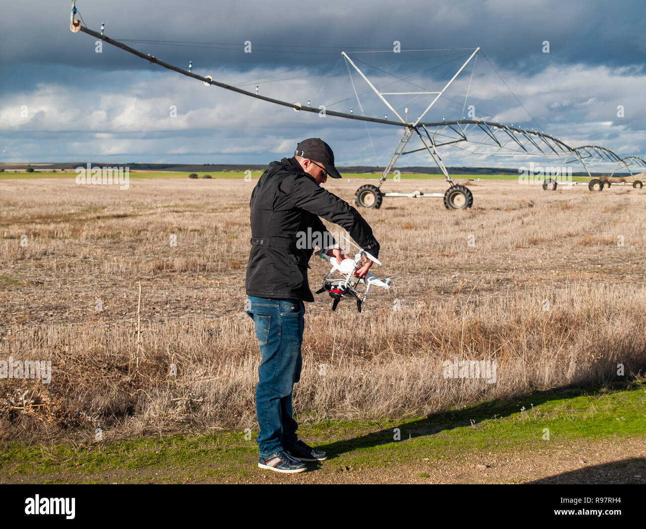 Un piloto de drone configurando su avión en un campo con y sistema de riego antes de volar Foto de stock