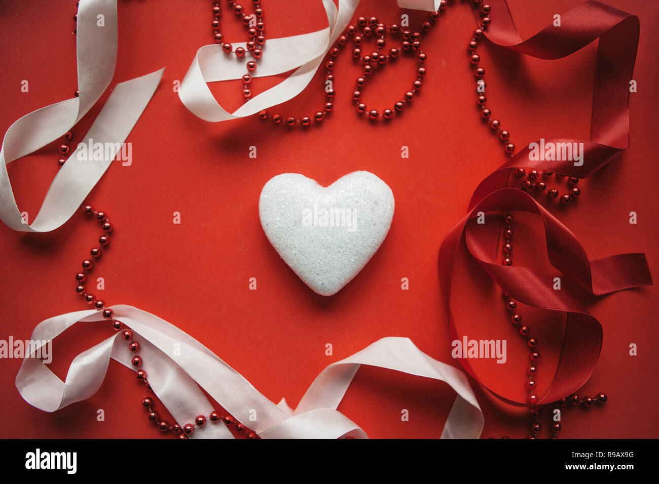 Corazón sobre un fondo rojo festivo decorado con cintas y cordones.  Concepto de Día de San Valentín o el día de la mujer u otro evento de amor  Fotografía de stock -