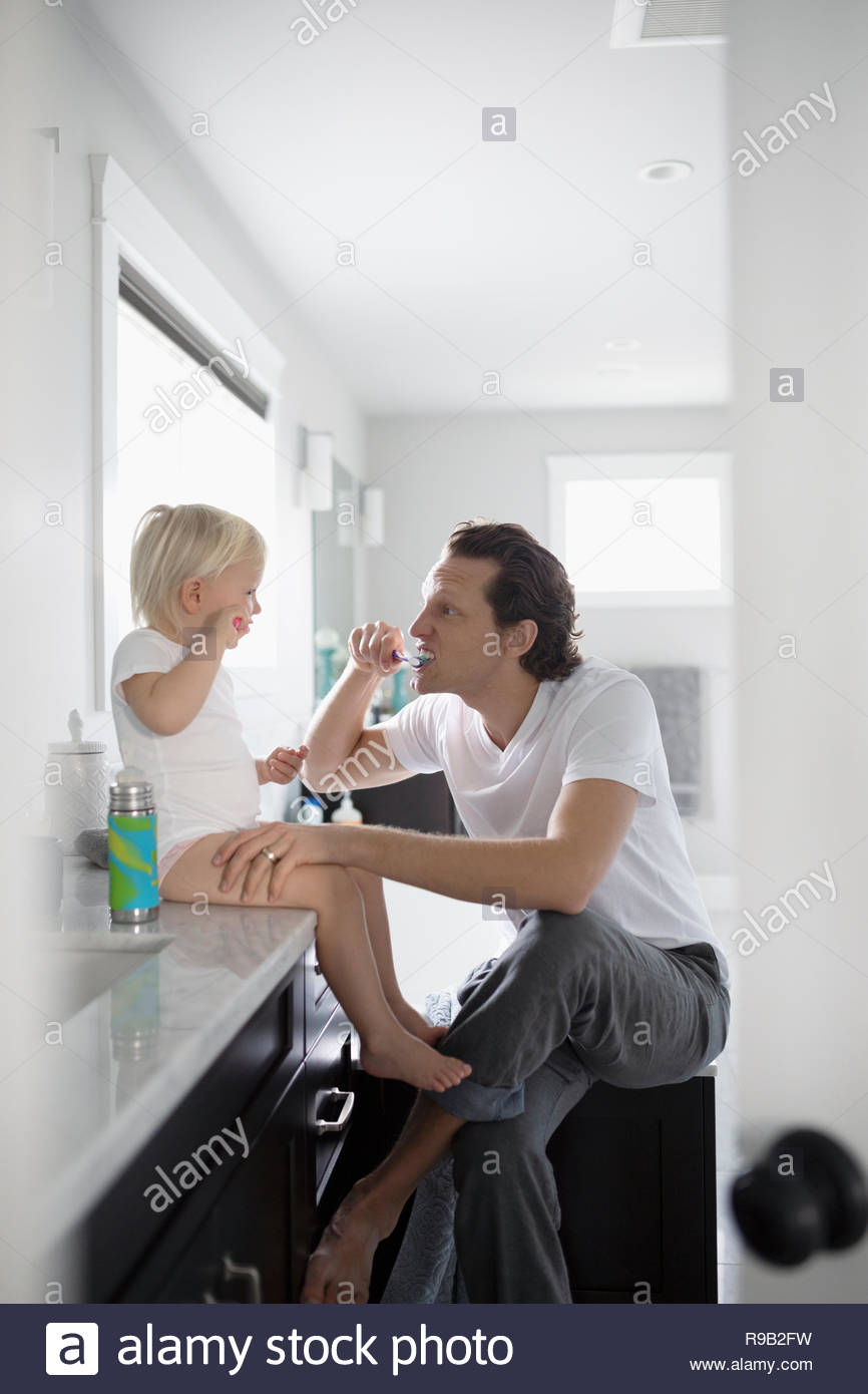Padre hija infante docente cómo cepillarse los dientes en el baño. Foto de stock
