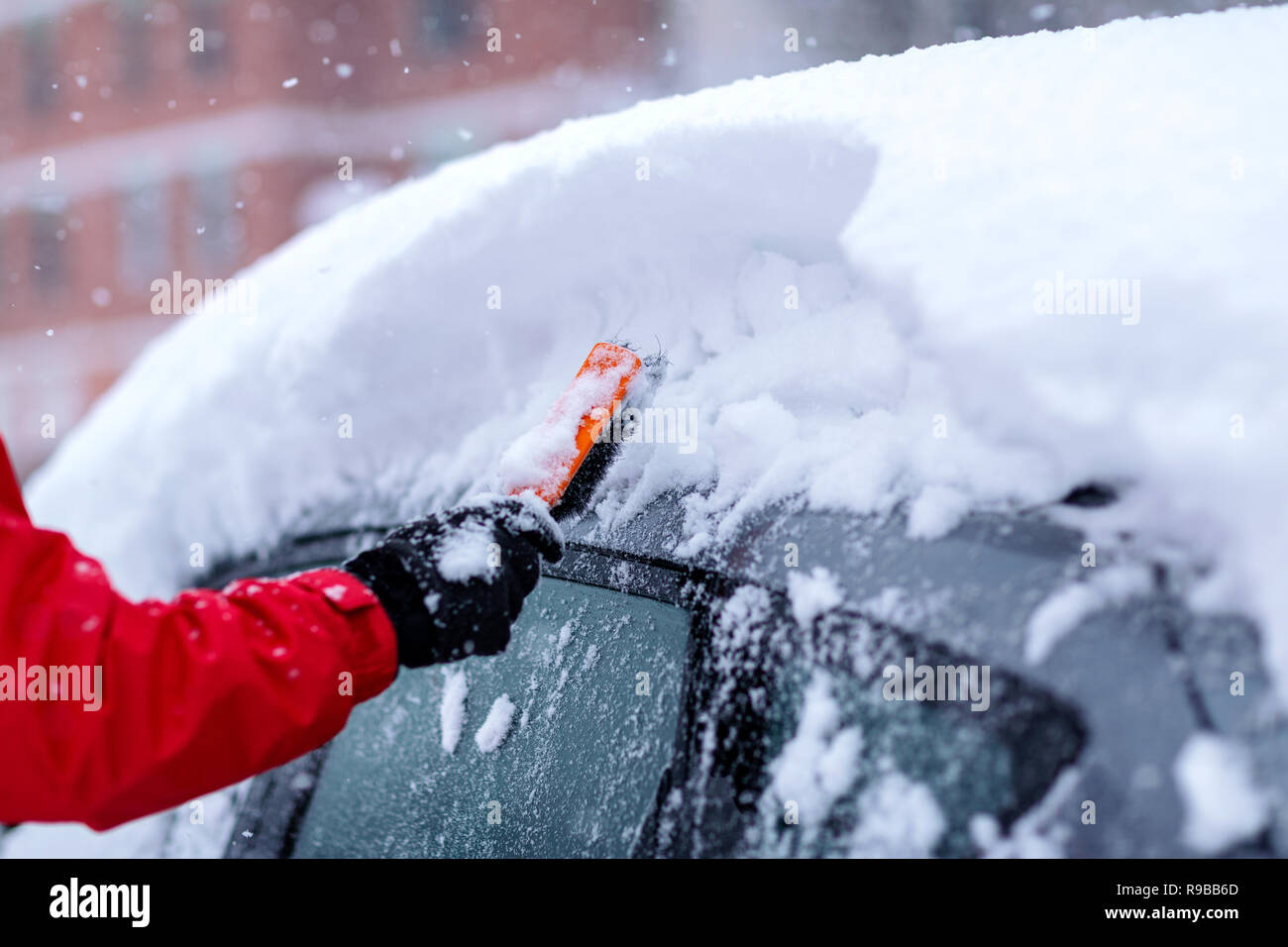 Transporte, el invierno, el clima, la gente y el concepto de vehículo - joven limpieza de nieve desde el coche con cepillo Foto de stock
