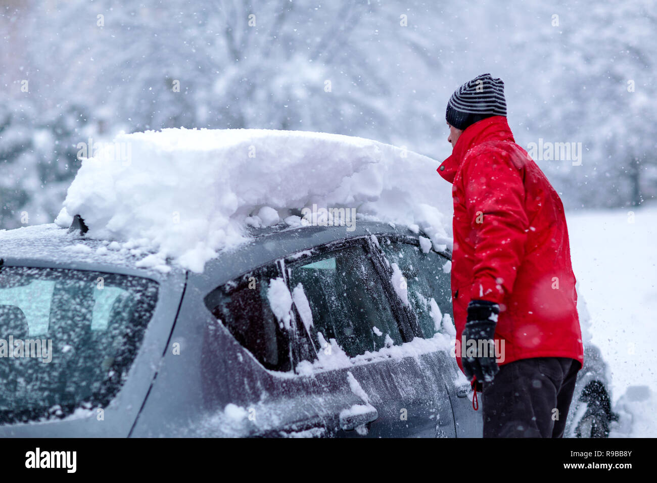Joven es limpiar limpiar su coche de nieve con pincel. Parking cubierto de nieve. Limpieza de nieve pesada Coche bajo la nieve intensas nevadas. Foto de stock