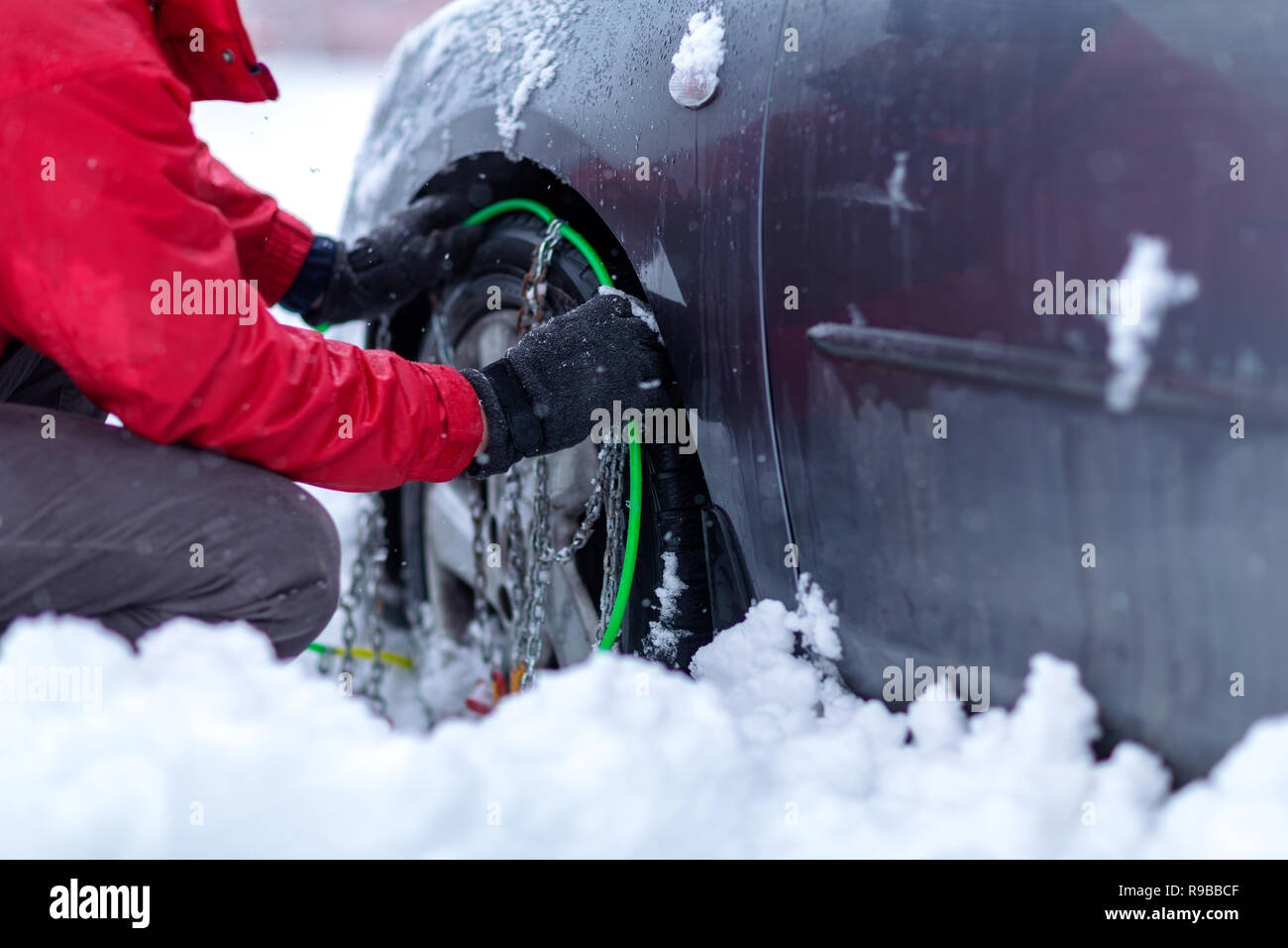 Cadenas para nieve en las ruedas del coche. joven intenta poner cadenas para la nieve en las llantas agarrando las cadenas para la nieve. Foto de stock