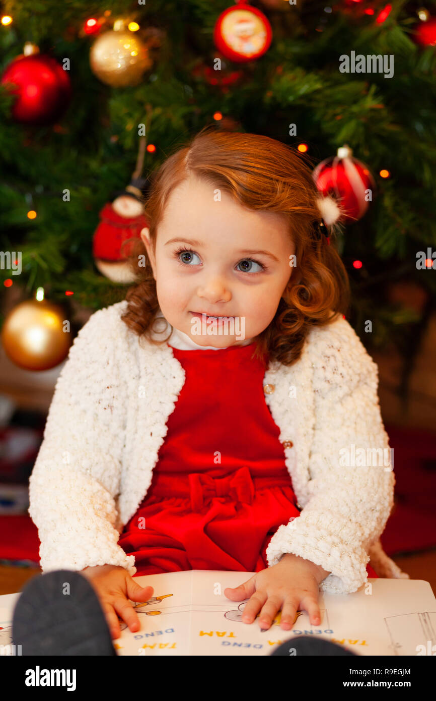 Retrato de una hermosa niña con vestido rojo cerca del árbol de Navidad. Foto de stock