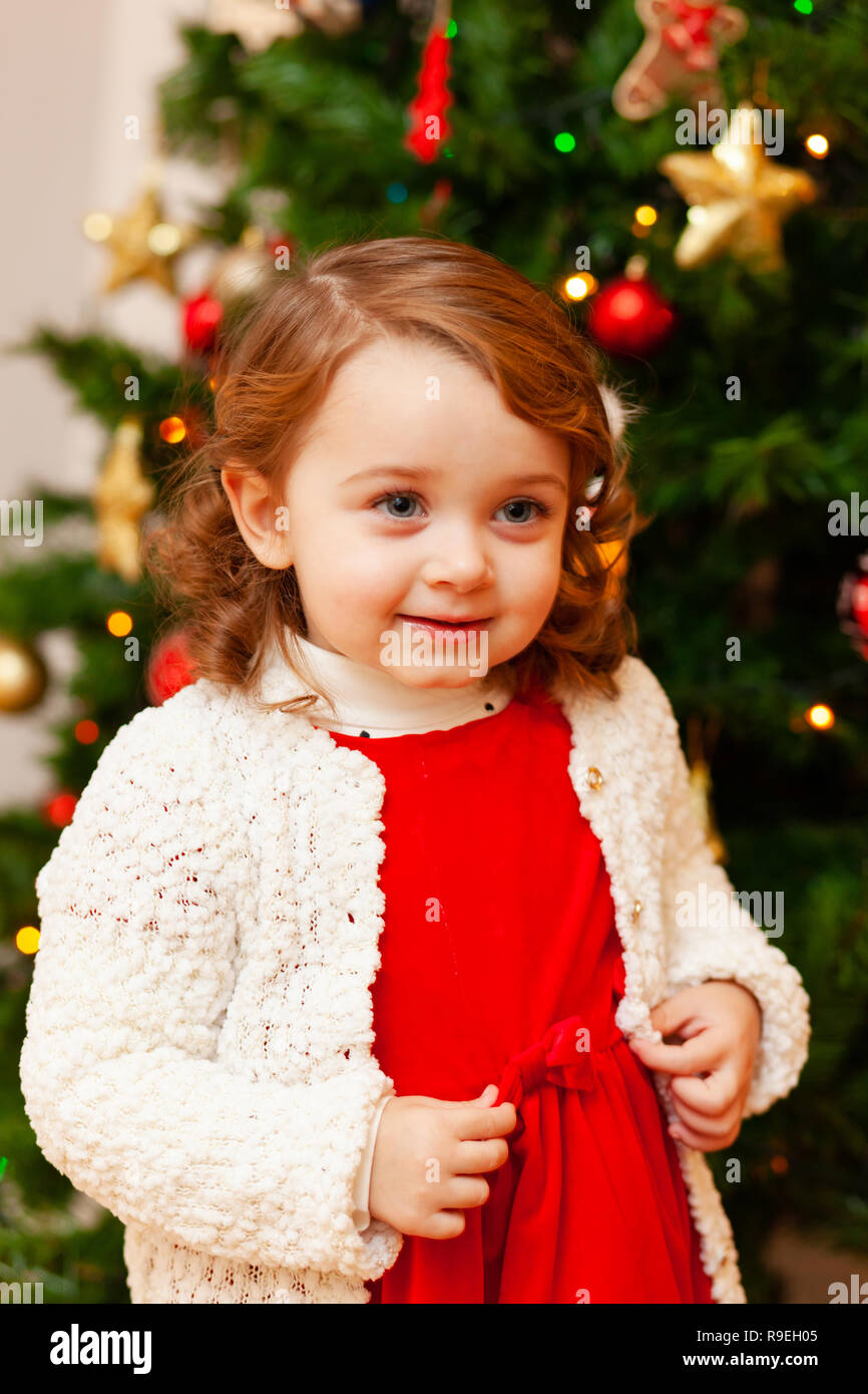 Retrato de una hermosa niña con vestido rojo cerca del árbol de Navidad. Foto de stock