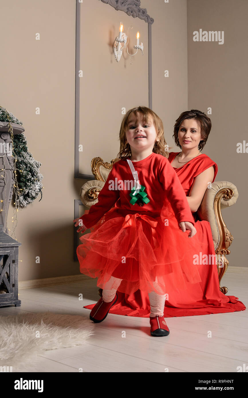 Feliz madre joven sostiene en las manos de su lindo bebé niña en  festividades de Navidad y Año Nuevo Niño con mamá en vestidos rojos en el  salón decorado con C Fotografía
