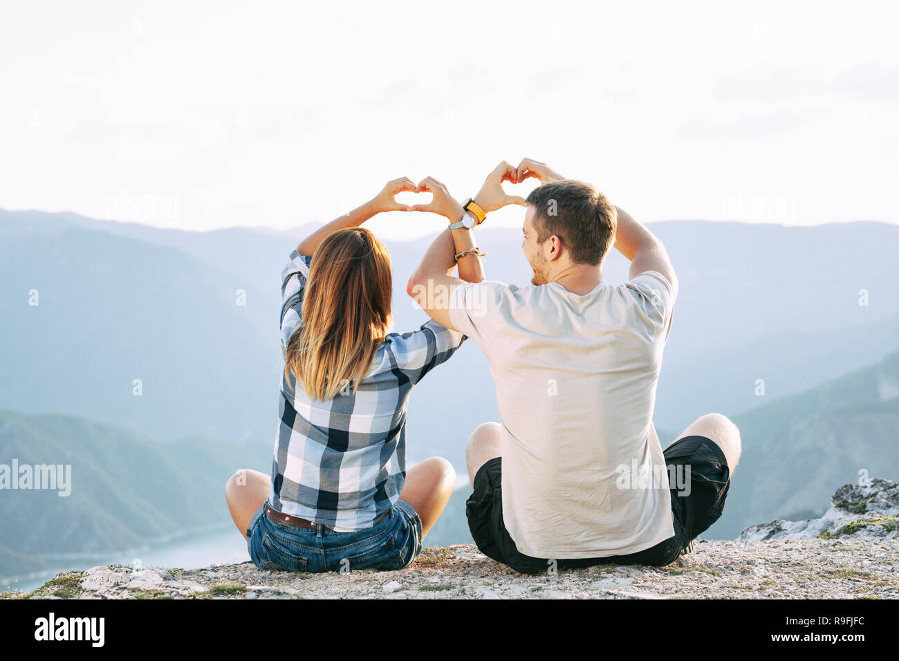 Pareja haciendo el amor en los corazones con sus manos cruzadas mientras están sentados en el suelo con una vista al lago Foto de stock