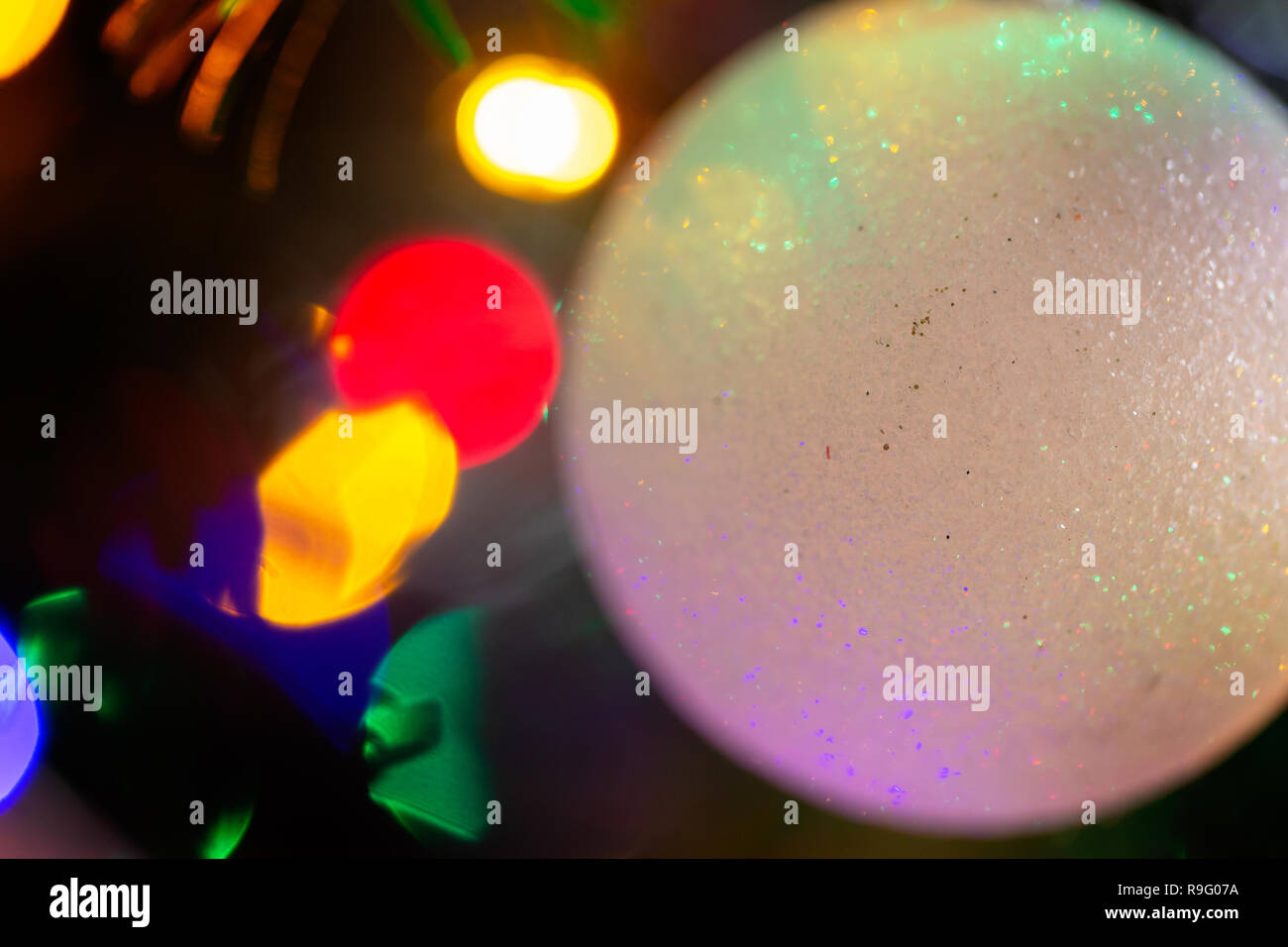 Cierre de un blanco, frosty bola delante de coloridas luces en un árbol de Navidad Foto de stock