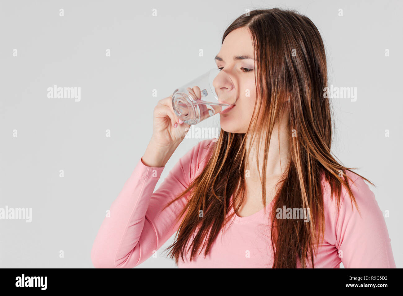 Joven morenita mujer bebiendo agua pura aislado sobre fondo gris Foto de stock