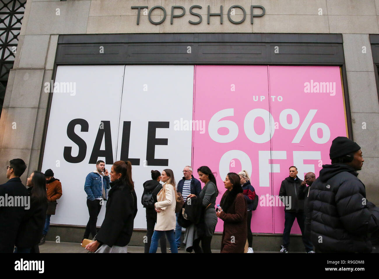 Los compradores son vistos de pie delante de un gran cartel de venta en la  ventana tienda Topshop de Londres, Oxford Street. Los compradores de  Navidad de última hora aproveche de pre-Navidad