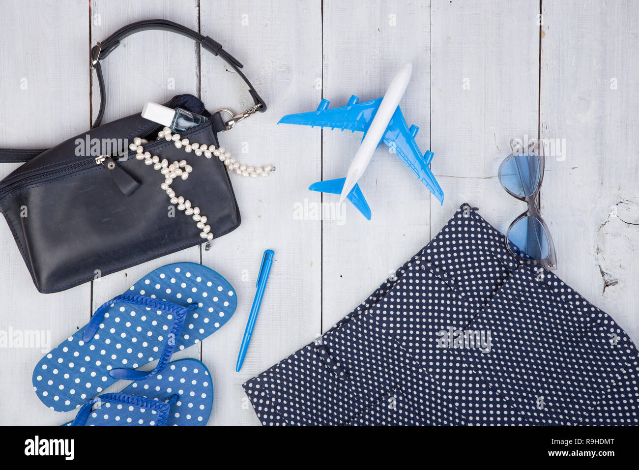 Concepto de viaje - verano la moda femenina con bolsa azul, gafas,  chanclas, el esmalte de uñas y poco avión sobre fondo blanco de madera  Fotografía de stock - Alamy