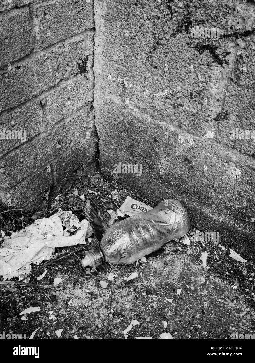 PTFE blanco botella bebidas de plástico desechados en las zonas urbanas de Backstreet. Metáfora plástica contaminación, guerra de residuos plásticos. Versión monocroma de R9KJNY. Foto de stock