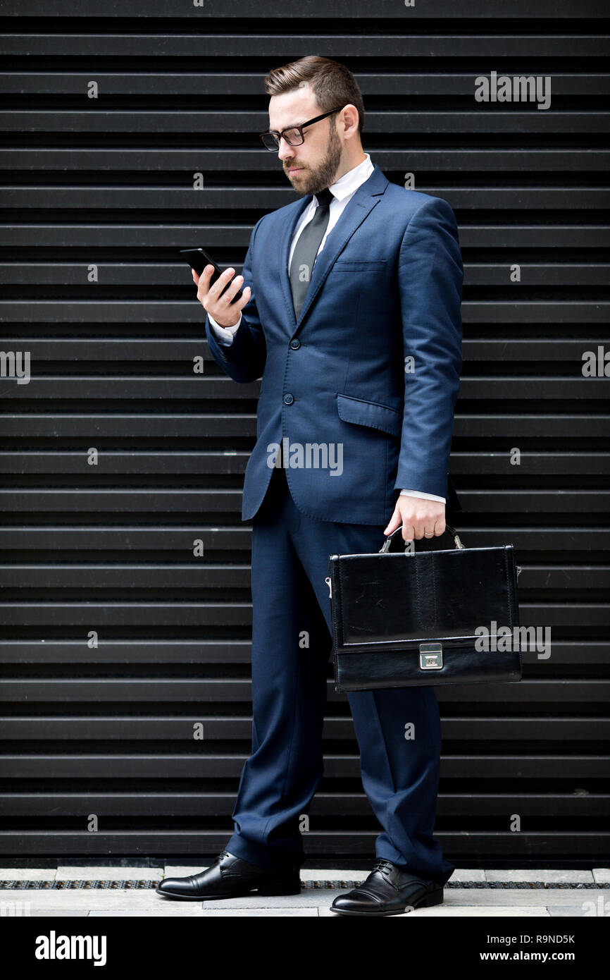 Hombre de negocios concentrado con el smartphone y el maletín Foto de stock