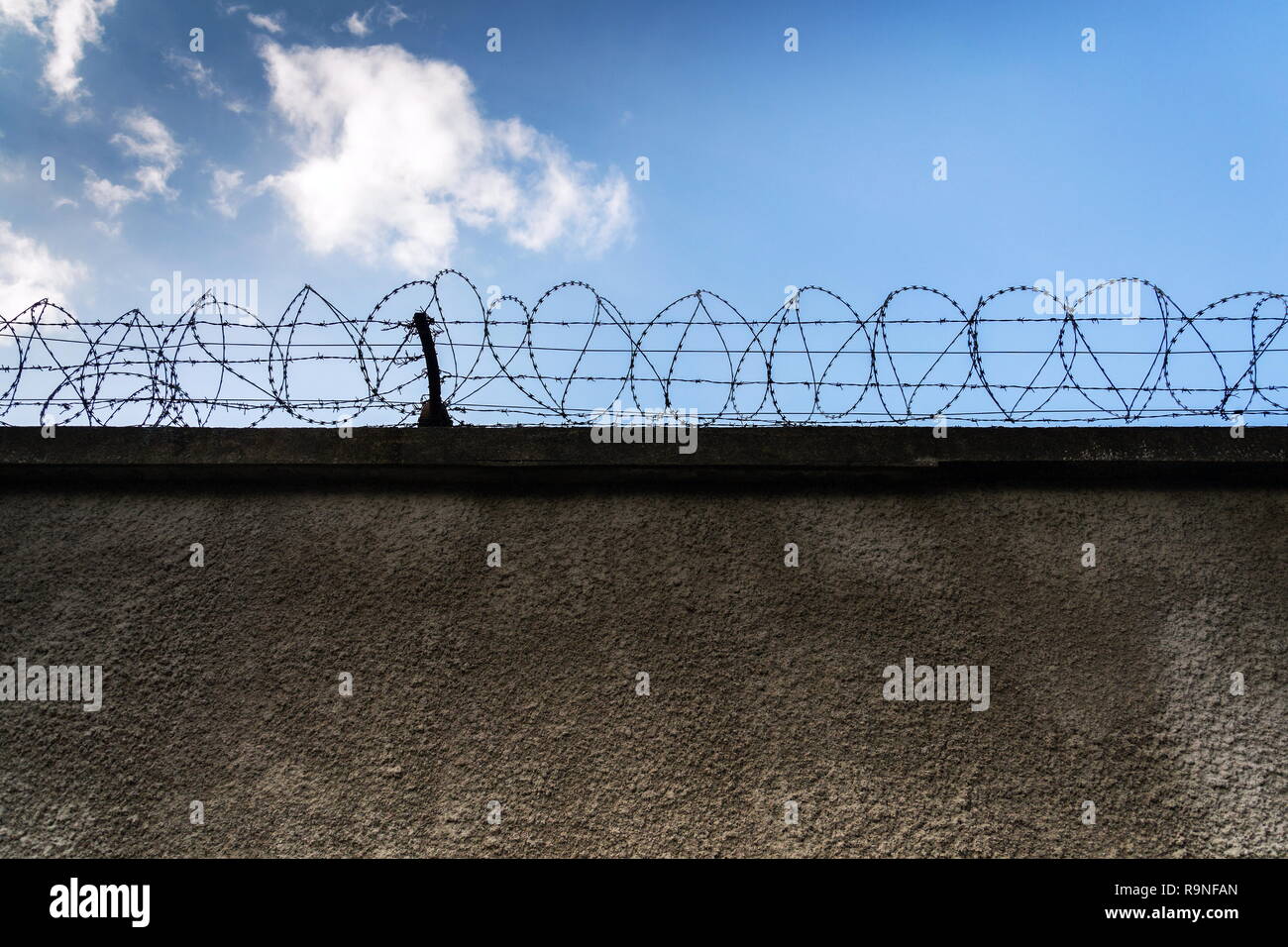 Valla de alambre de espino alrededor de los muros de la cárcel, azul cielo nublado en el fondo, la seguridad, la delincuencia o la inmigración ilegal, concepto Foto de stock