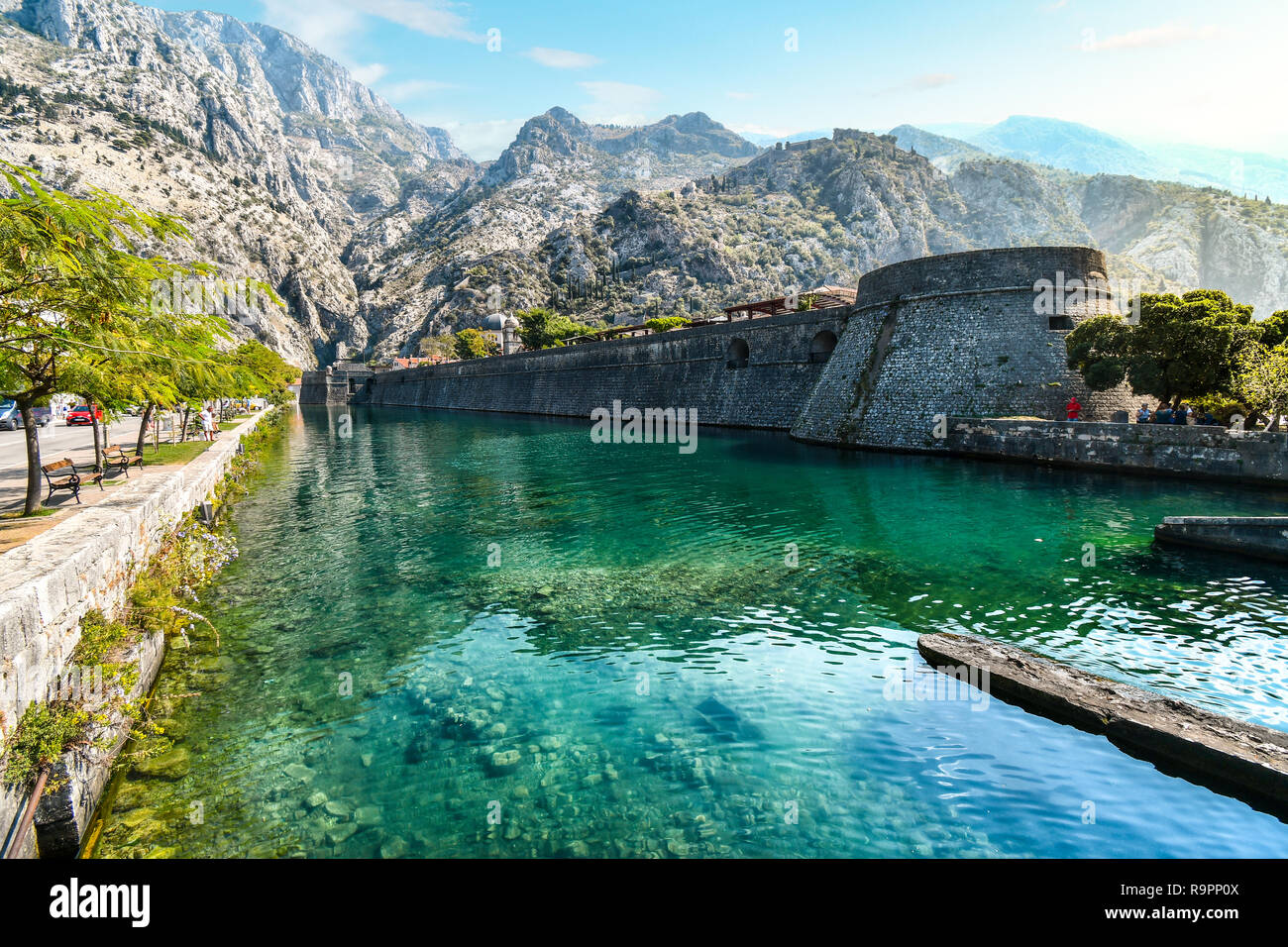 Las murallas medievales de la ciudad y el foso que separa a las montañas y el castillo detrás en el Adriático, antigua ciudad de Kotor, Montenegro. Foto de stock