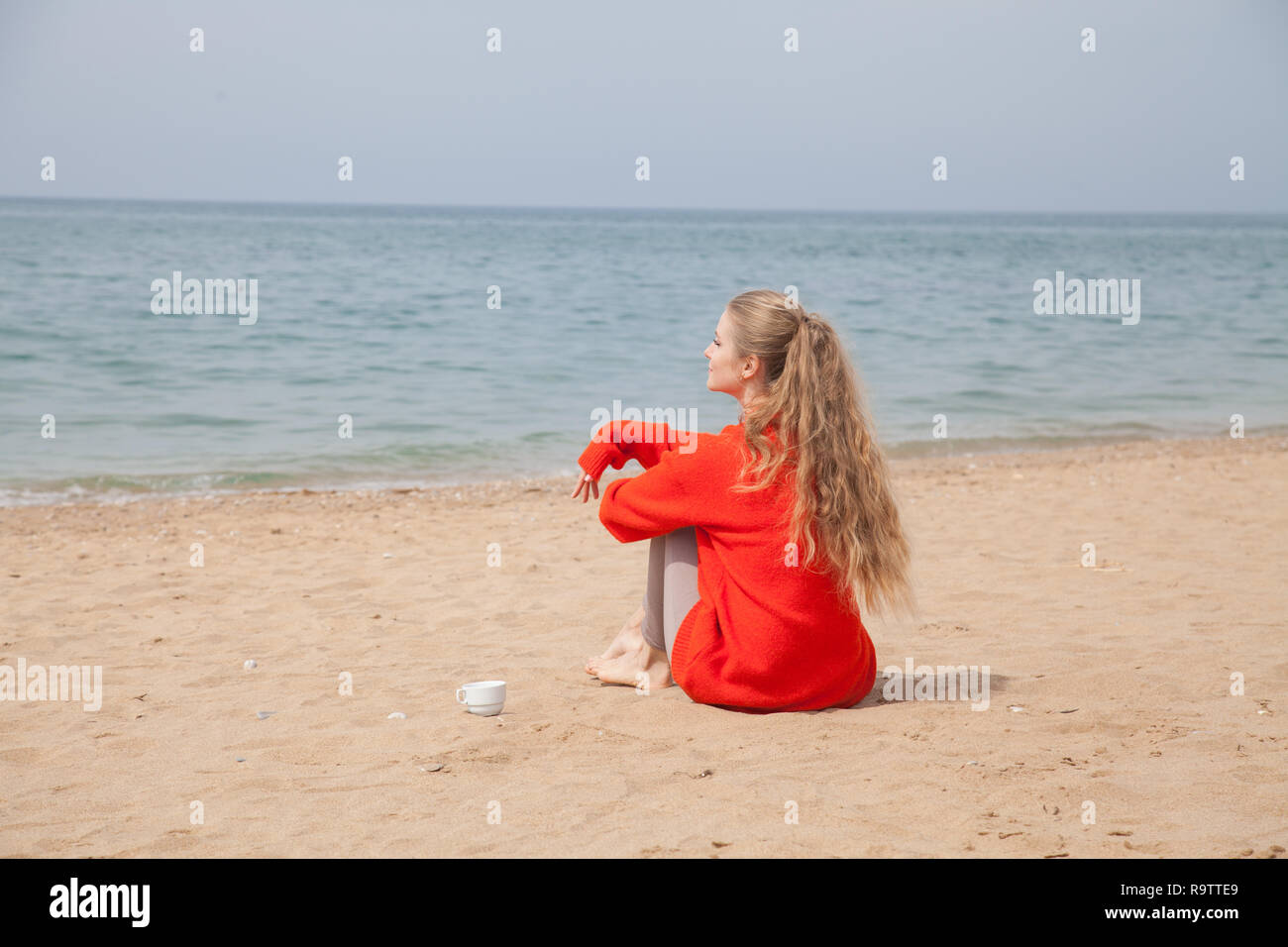 Una mujer sentada en una playa desierta mirando el mar bebedores de té Foto de stock