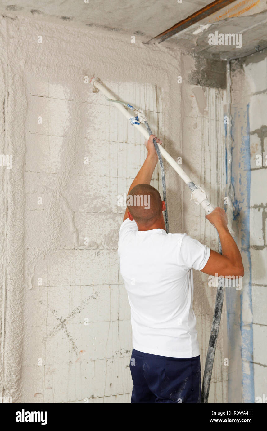 El trabajador está colocando un enlucido de yeso en una pared. está usando  una paleta larga.