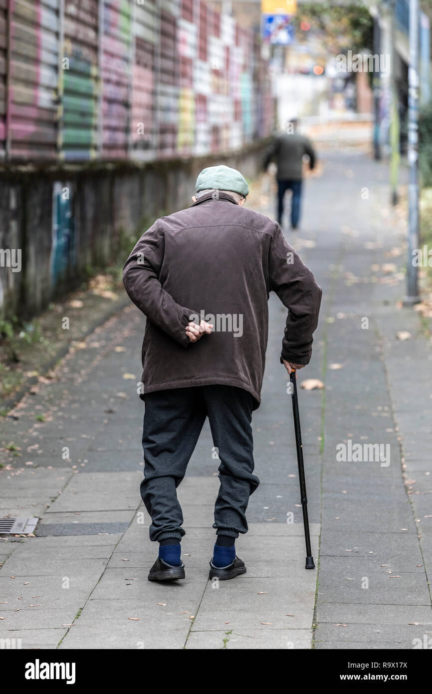 Viejo hombre camina despacio, apoyándose en un bastón, Foto de stock