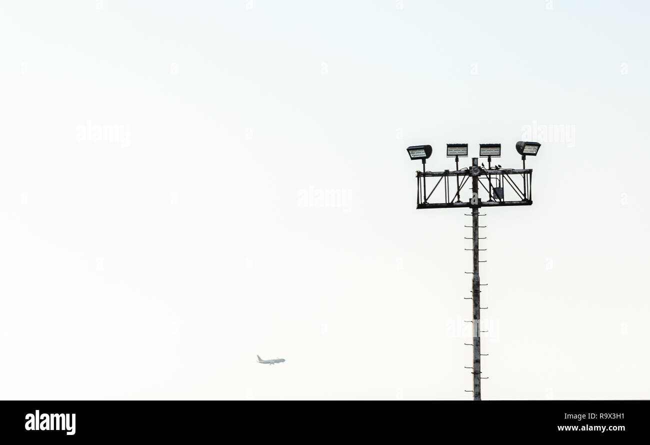 Poste de luz altos con luces en la parte superior y un avión en la distancia Foto de stock