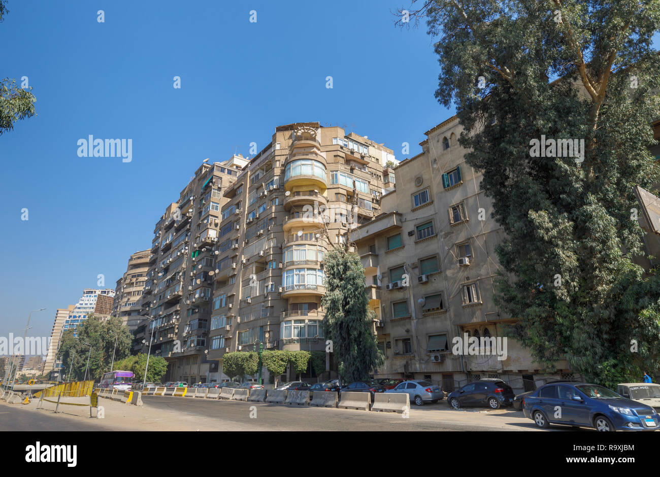 Escena callejera en Giza, en El Cairo, Egipto con grande típico bloque de apartamentos residenciales en carretera con antenas parabólicas y unidades de aire acondicionado exterior Foto de stock