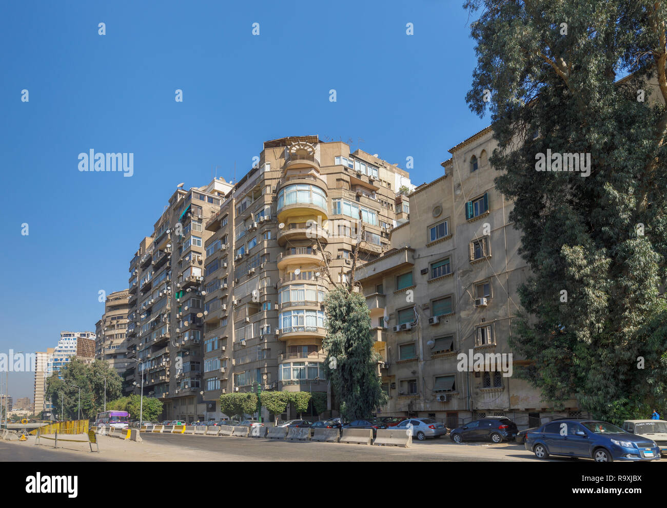 Escena callejera en Giza, en El Cairo, Egipto con grande típico bloque de apartamentos residenciales en carretera con antenas parabólicas y unidades de aire acondicionado exterior Foto de stock