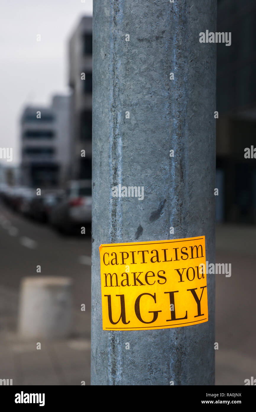 Adhesivo en un poste de la luz en el distrito financiero, con un texto que dice: "el capitalismo le hace feos' Foto de stock