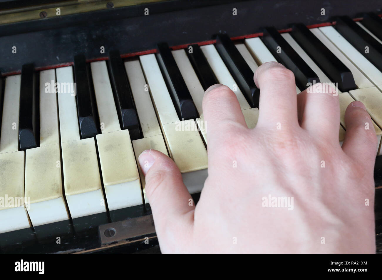 Una mano derecha jugando una E (mi) acorde mayor en un viejo piano negro  con amarillentas teclas agrietado, pulsando el botón E (mi), G# diesis  (SOL#), B (SI) notas Fotografía de stock -