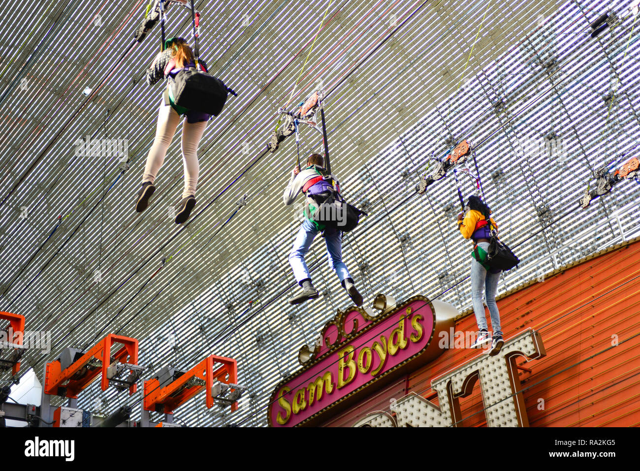 Tres personas cuelgan del techo de bóveda de cañón en Fremont Street Experience mientras vuelan la atracción SlotZilla Zip Line en Las Vegas NV Foto de stock