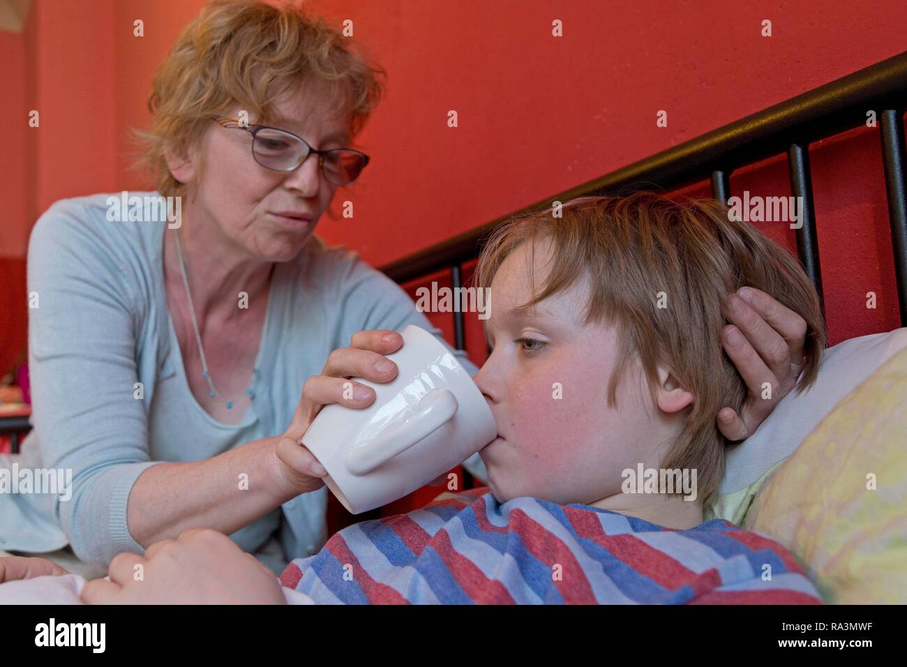 La madre cuida del hijo enfermo en la cama, símbolo de imagen, frío, cuidado, padres de familia, infancia, Alemania Foto de stock