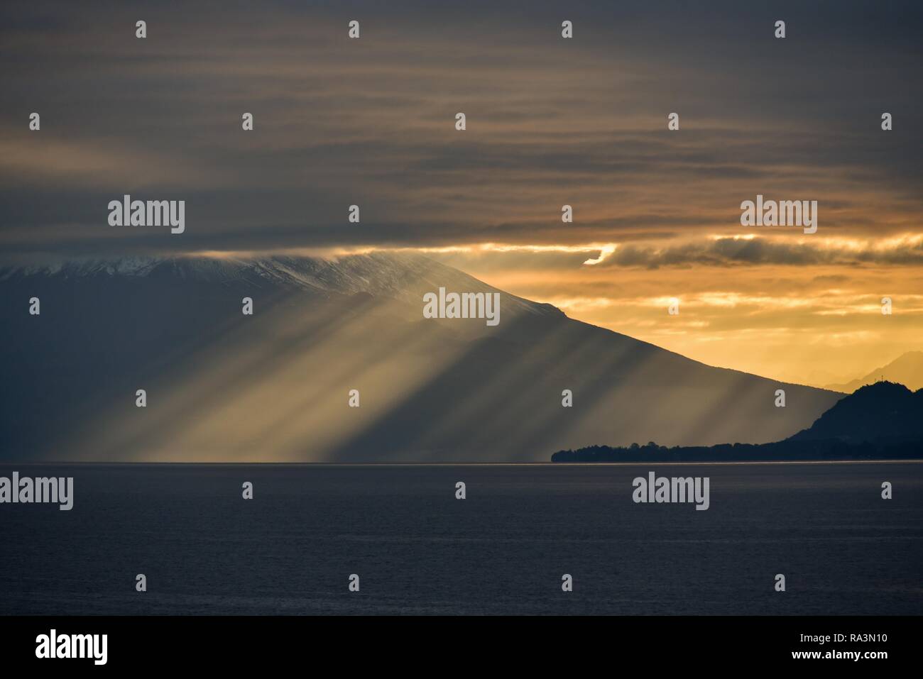 Los rayos del sol brillan a través de oscuro cielo nublado frente al volcán Osorno en el Lago Llanquihue, amanecer, Puerto Varas, Carretera Austral Foto de stock