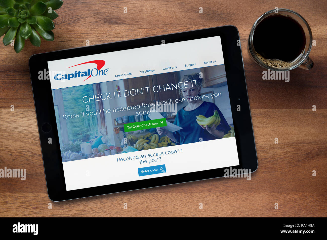 El sitio web de Capital One se ha visto en un iPad, en una mesa de madera junto con un café espresso y una planta de casa (Editorial). Foto de stock