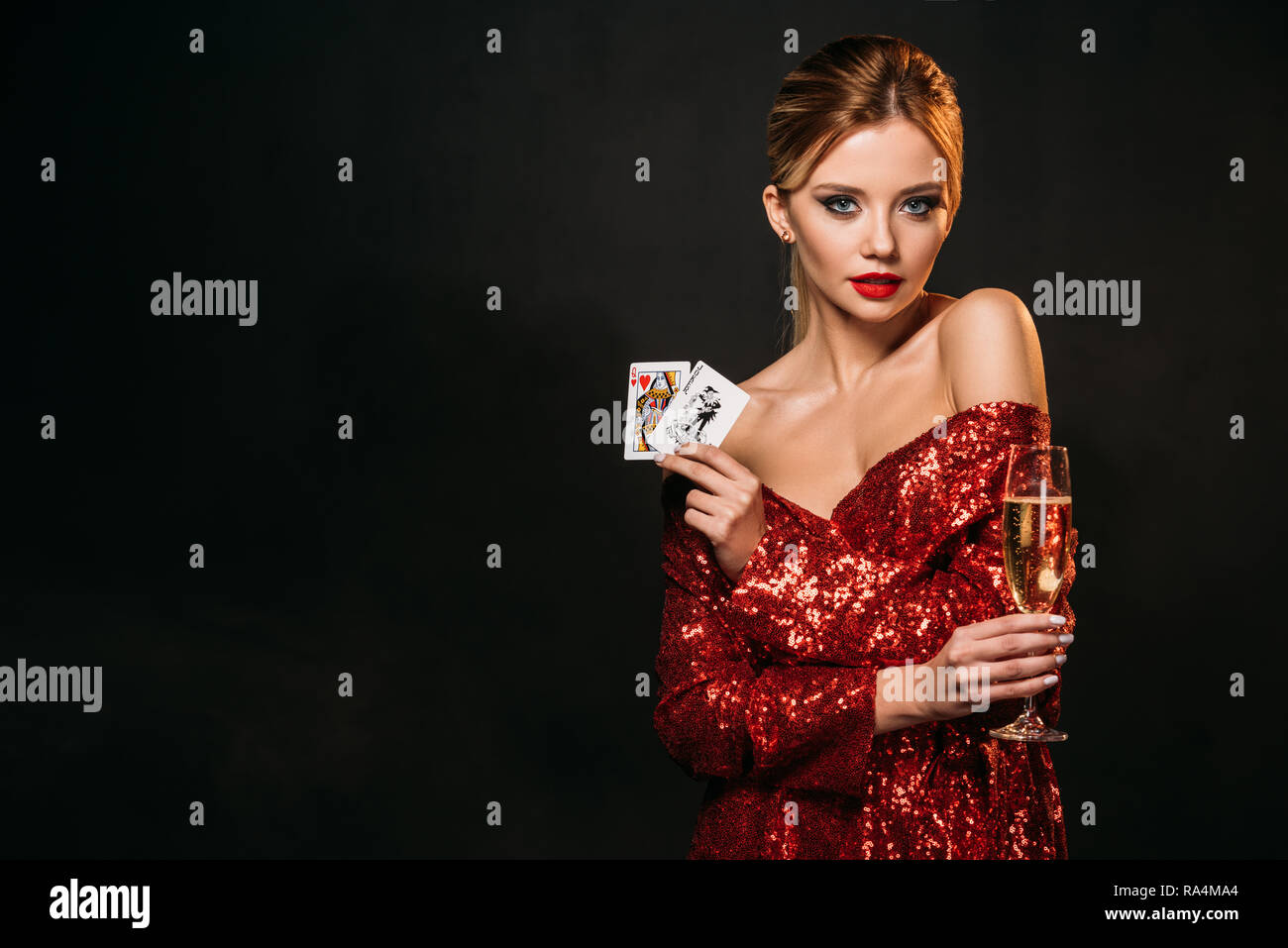 Atractiva chica en vestido rojo celebración bromista y reina de corazones aislados de tarjetas en negro, mirando a la cámara Fotografía de stock - Alamy