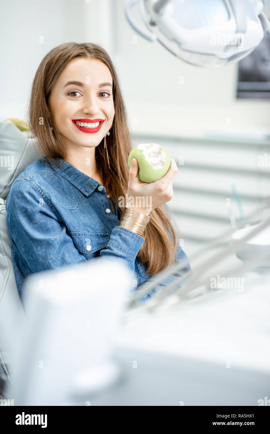 Retrato de una joven mujer hermosa con sonrisa saludable sentado con manzana verde en la oficina dental Foto de stock