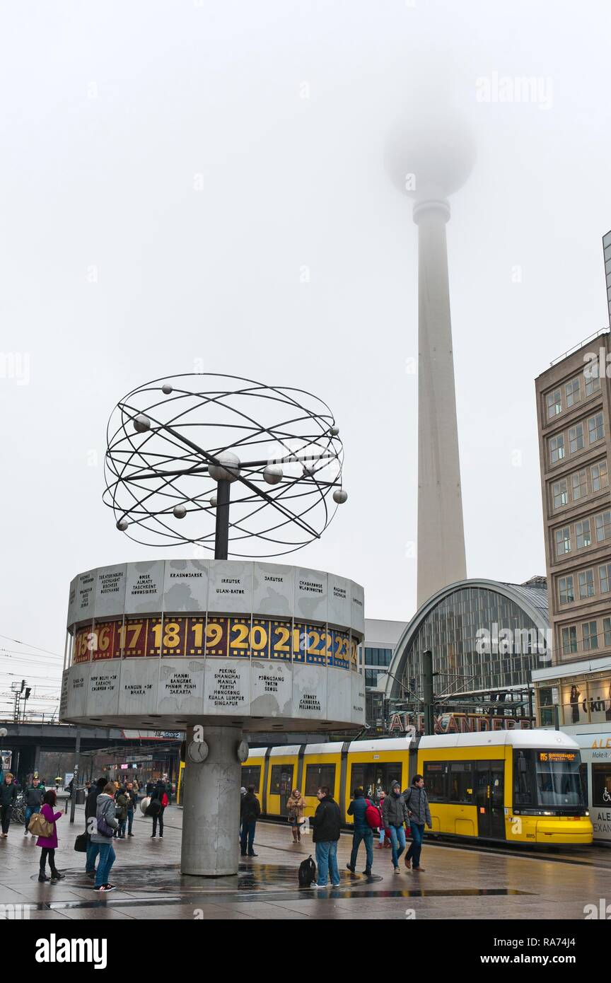 Reloj con horario mundial, amarillo tren-tranvía, la torre de TV en la niebla, Alex, Alexanderplatz, Berlin Mitte, Berlin, Alemania Foto de stock