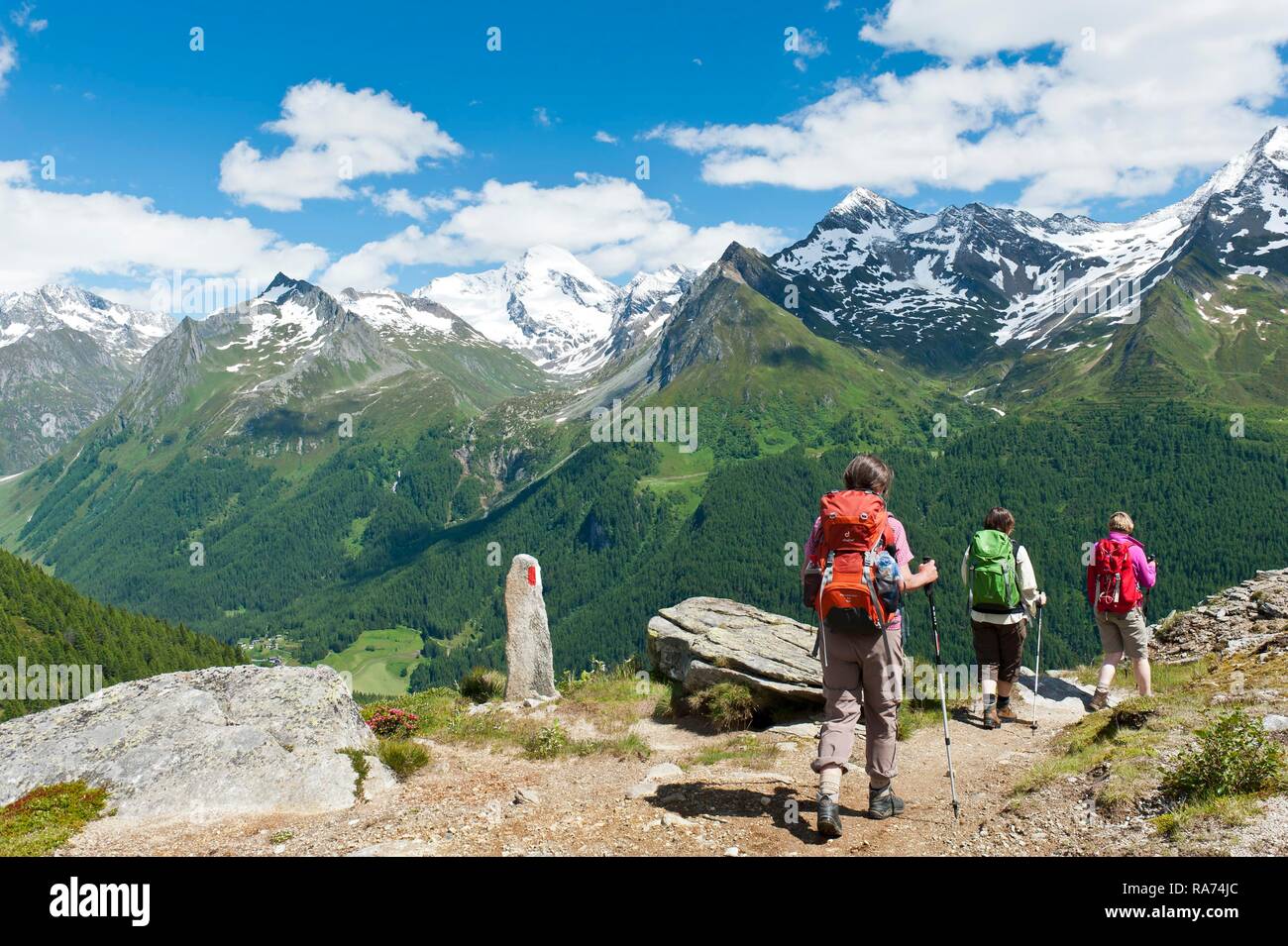 Tres excursionistas caminata por un sendero de trekking, marcas rojas y blancas de piedra, montañas cubiertas de nieve, cerca del Alm, Kasern Waldner Foto de stock