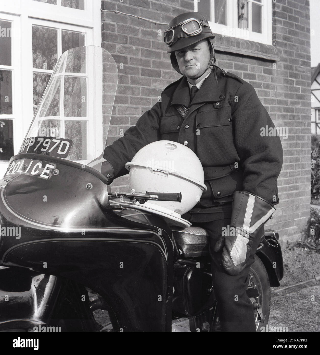 1967, la policía británica con casco y googles sentado en una motocicleta de la policía, fuera de una casa, con un hogar hecho "plato volador" en su regazo, Inglaterra, Reino Unido. A finales de los '60s Bretaña experimentó un "OVNI de la locura, alentado por programas de televisión populares tales como Dr Who y esta sierra mecánica de bricolaje muchos intenta crear su propio. Foto de stock