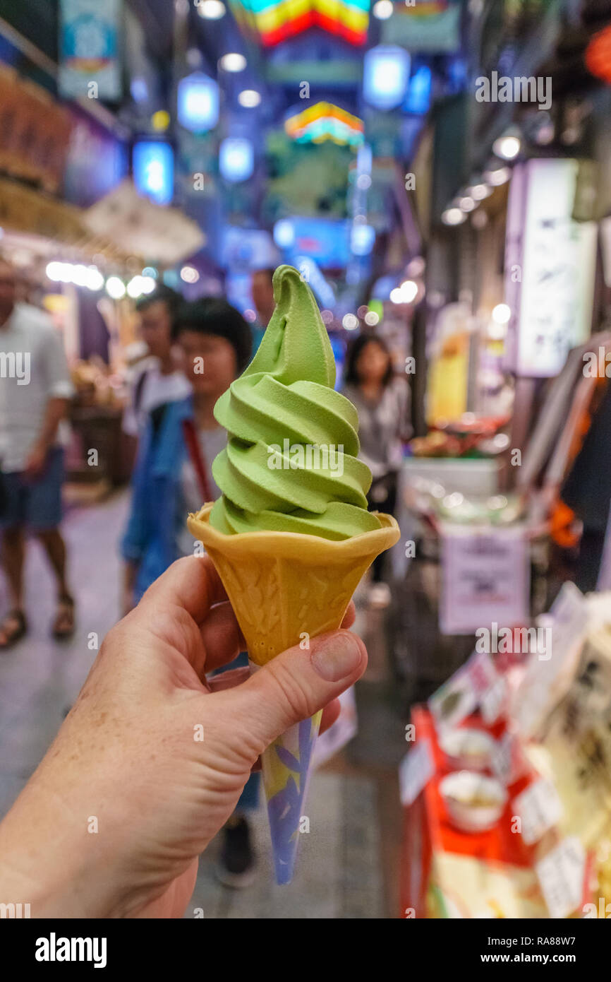 Cerca de mano sujetando verde suave servir el té verde matcha o cono de helado en el mercado de comida Japonesa Foto de stock