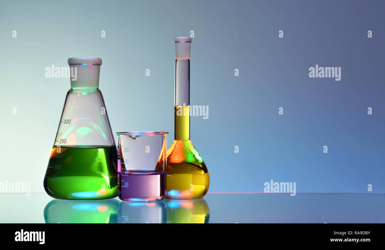 El material de vidrio de laboratorio con coloridos líquidos y productos químicos sobre fondo azul. Foto de stock