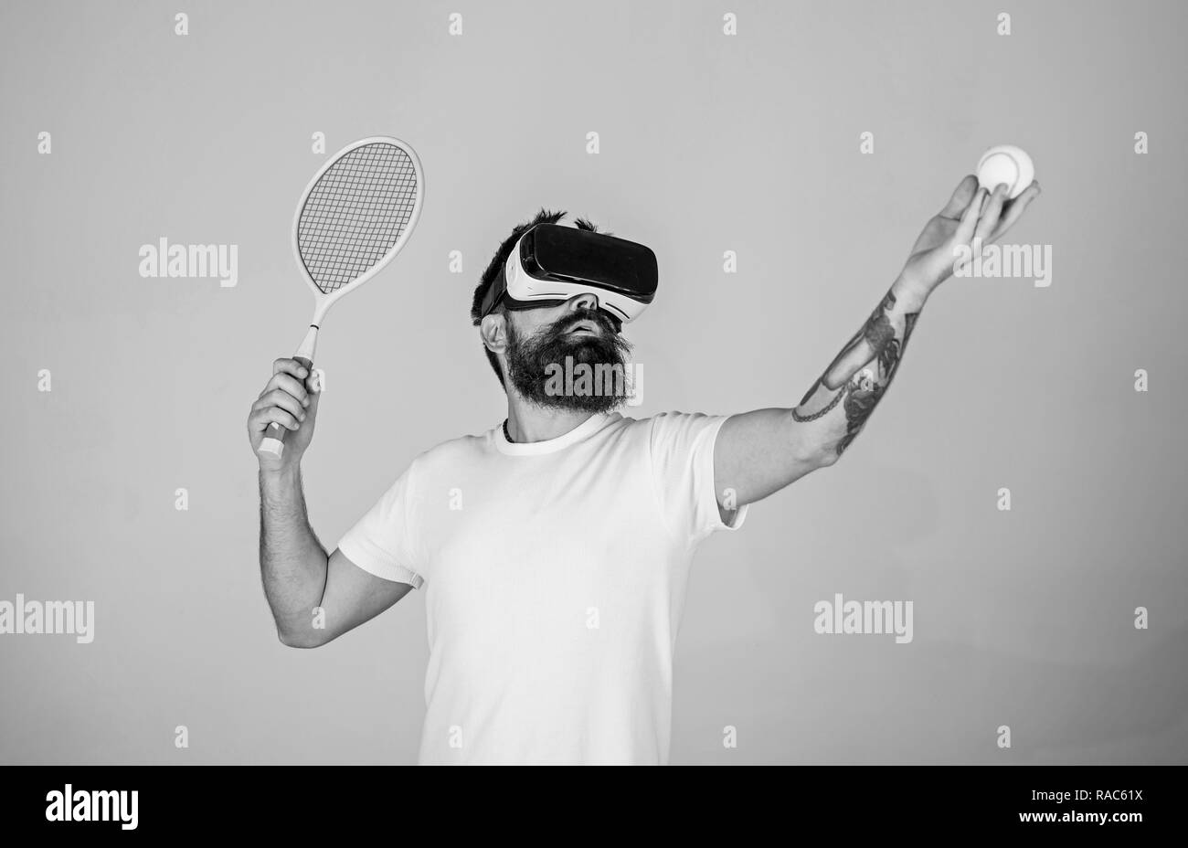 Guapo en casco de realidad virtual jugando al tenis, fondo gris. Hipster  utilizan tecnología moderna para juegos de deportes. Chico con gafas VR jugar  tenis con la raqueta y la bola. Concepto