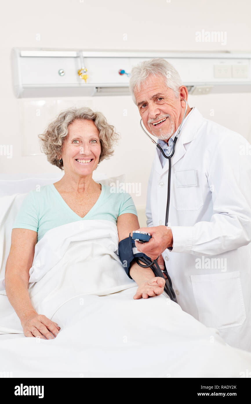 Hombre como jefe médico en la medición de la presión sanguínea en una persona de la tercera edad en el hospital Foto de stock