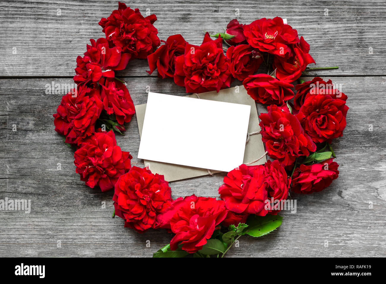 Rosas flores rojas en forma de corazón con tarjeta de felicitación en blanco sobre fondo de madera de estilo rústico. El día de San Valentín concepto. Vista superior de la maqueta. Foto de stock