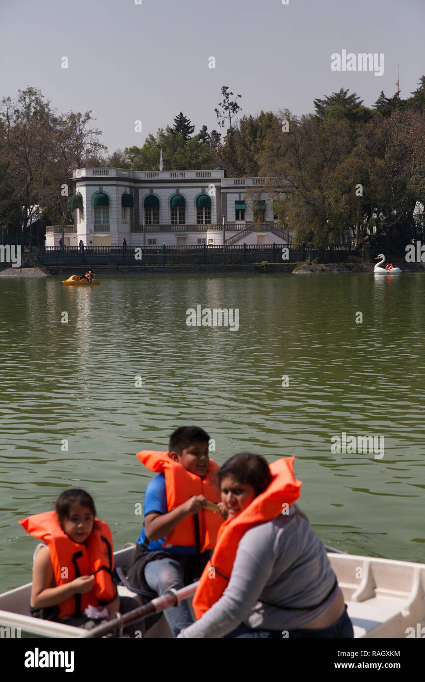 Una madre y sus dos hijos visten un chaleco de espuma cada como son paseos en bote en frente de la Casa del Lago artificial en el lago de Chapultepec en Mex Foto de stock