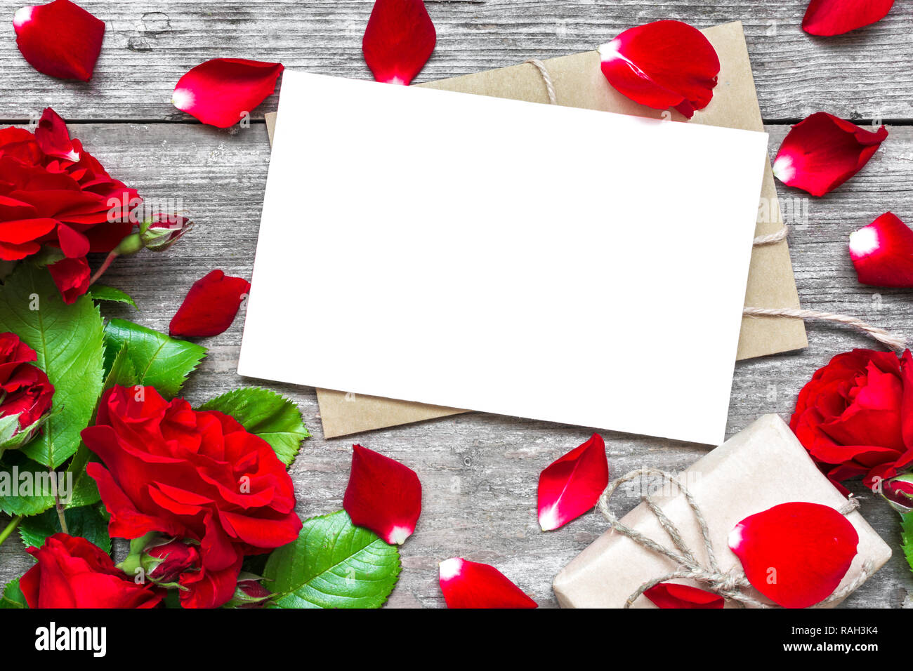 Día de San Valentín fondo. Tarjeta de felicitación en blanco con rosas rojas ramo de flores con pétalos y sobres y caja de regalo sobre fondo de madera de estilo rústico. Foto de stock